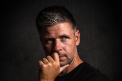 Portret van een zelfverzekerde man, met een vastberaden blik terwijl hij wegkijkt en zijn hand stoer onder zijn gezicht plaatst. Een krachtige en expressieve foto, ideaal voor het vastleggen van persoonlijkheid en karakter.