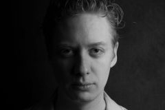 Zwart-wit portret van een man, met dramatisch licht dat zijn linkerzijde in schaduw en zijn rechterzijde in helder licht hult. Een stoere en expressieve foto die perfect is voor artistieke en professionele doeleinden.