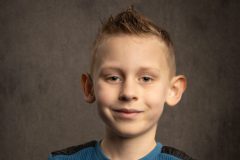 Portret van een stoere 7-jarige jongen met kort haar, met zijn handen over elkaar. Een levendige en zelfverzekerde pose, perfect voor familieherinneringen.